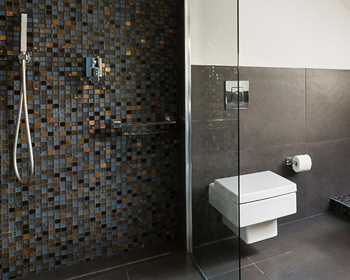 A wet room shower with dark mosaic tiles